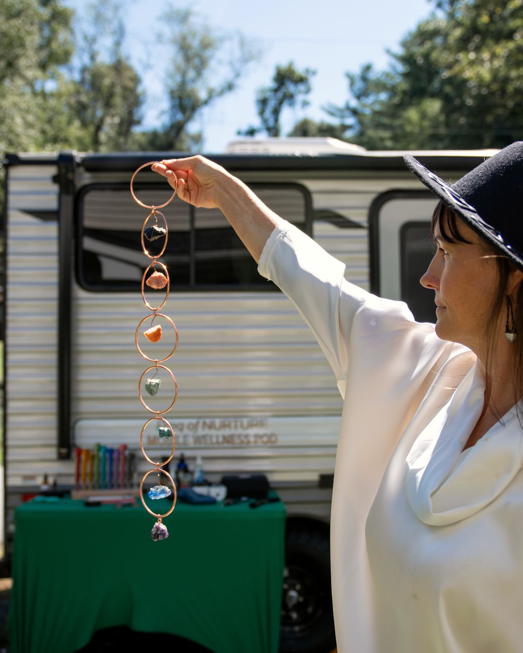 Ashley holds up a strand of crystals in the sunshine beside the Pod, a cloth-covered table set up alongside it.