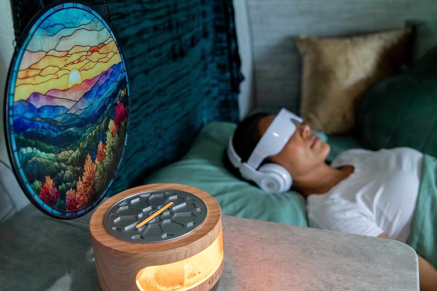 The stained-glass mountain panel and a glowing salt-lamp clock beside a guest resting under the BrainTap visor.