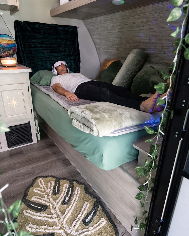 Looking in through the Pod’s open door: a guest in a white top resting on the mat, a monstera-leaf rug on the floor.