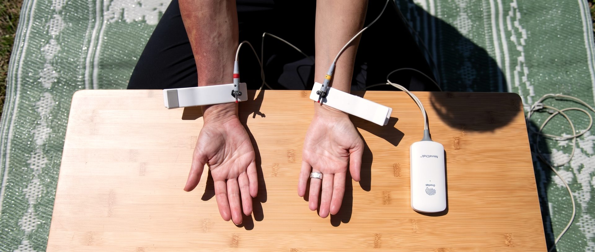 A guest’s hands rest palms-up on a bamboo board while two sensors read heart-rate variability at the wrists.