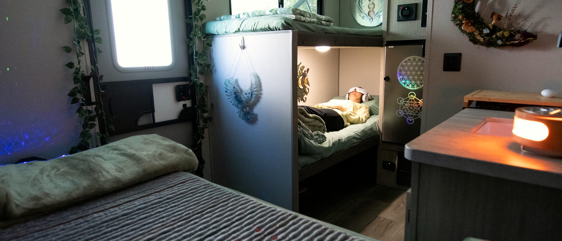 Inside the Pod: a guest resting in the bunk under soft light, the bed made up with sage linens in the foreground.
